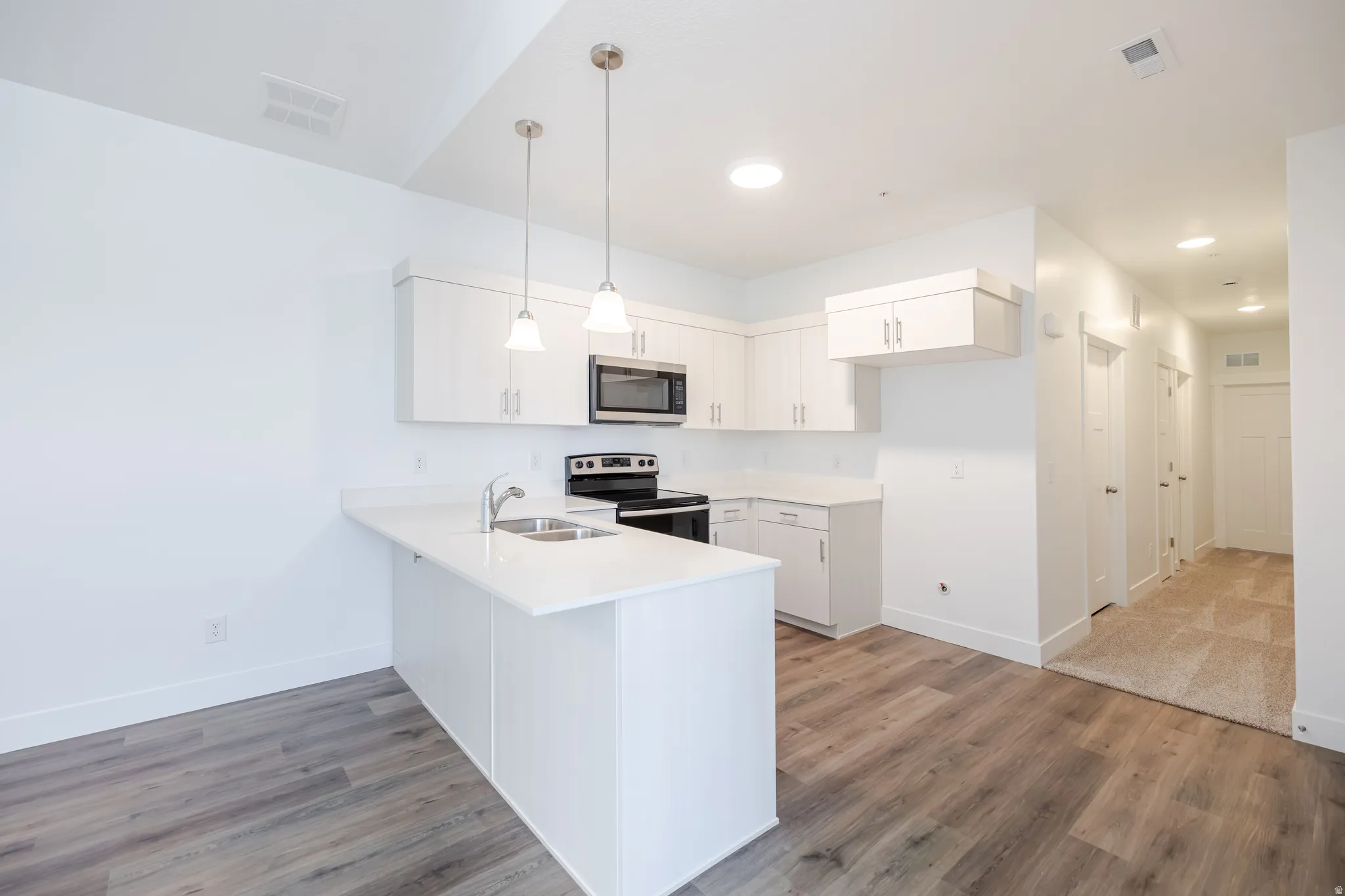 Contemporary kitchen featuring white cabinetry, stainless steel microwave, and pendant lighting