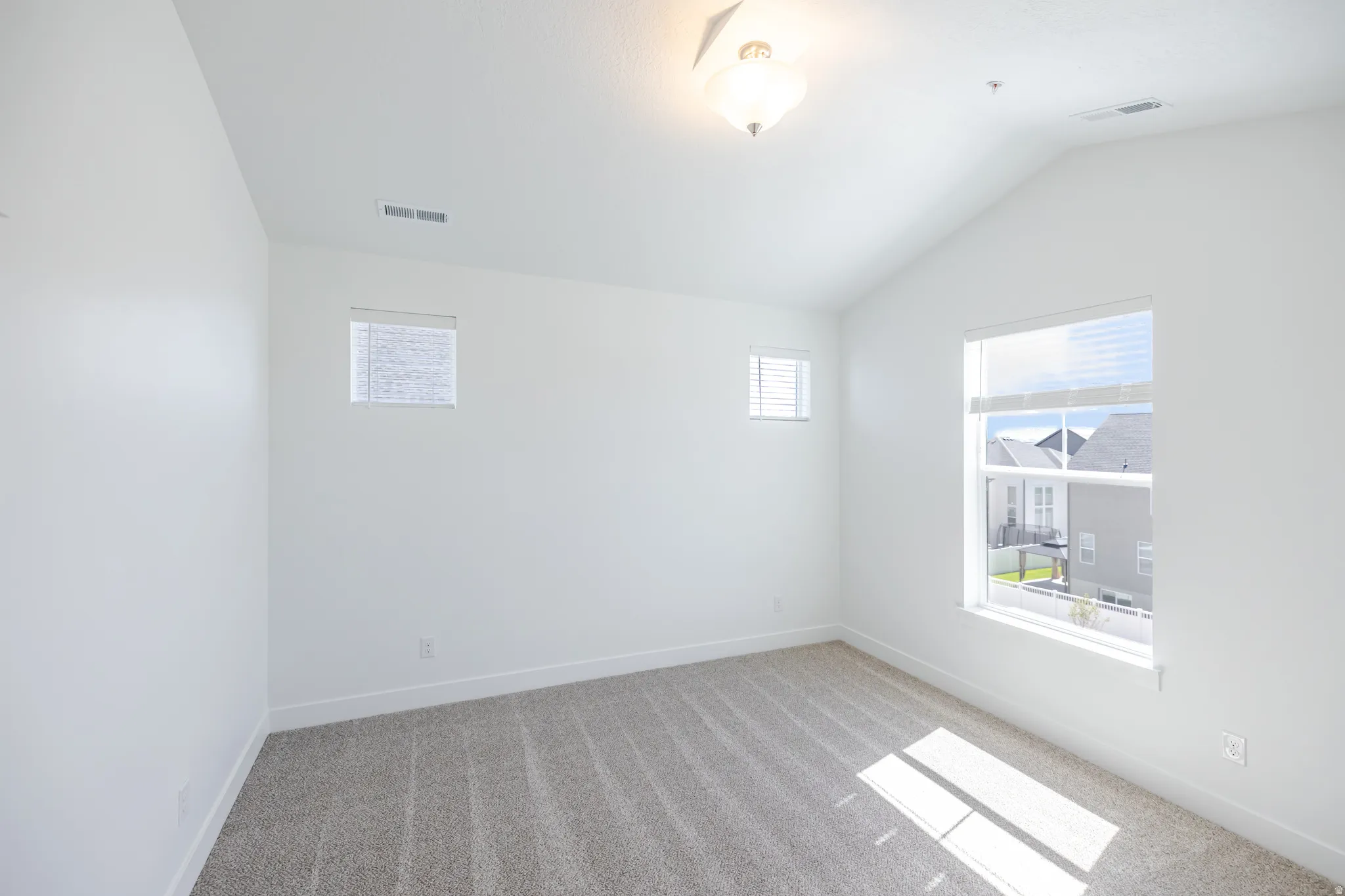 Vaulted ceiling room with neutral carpet, multiple windows, and a semi-flush mount light fixture