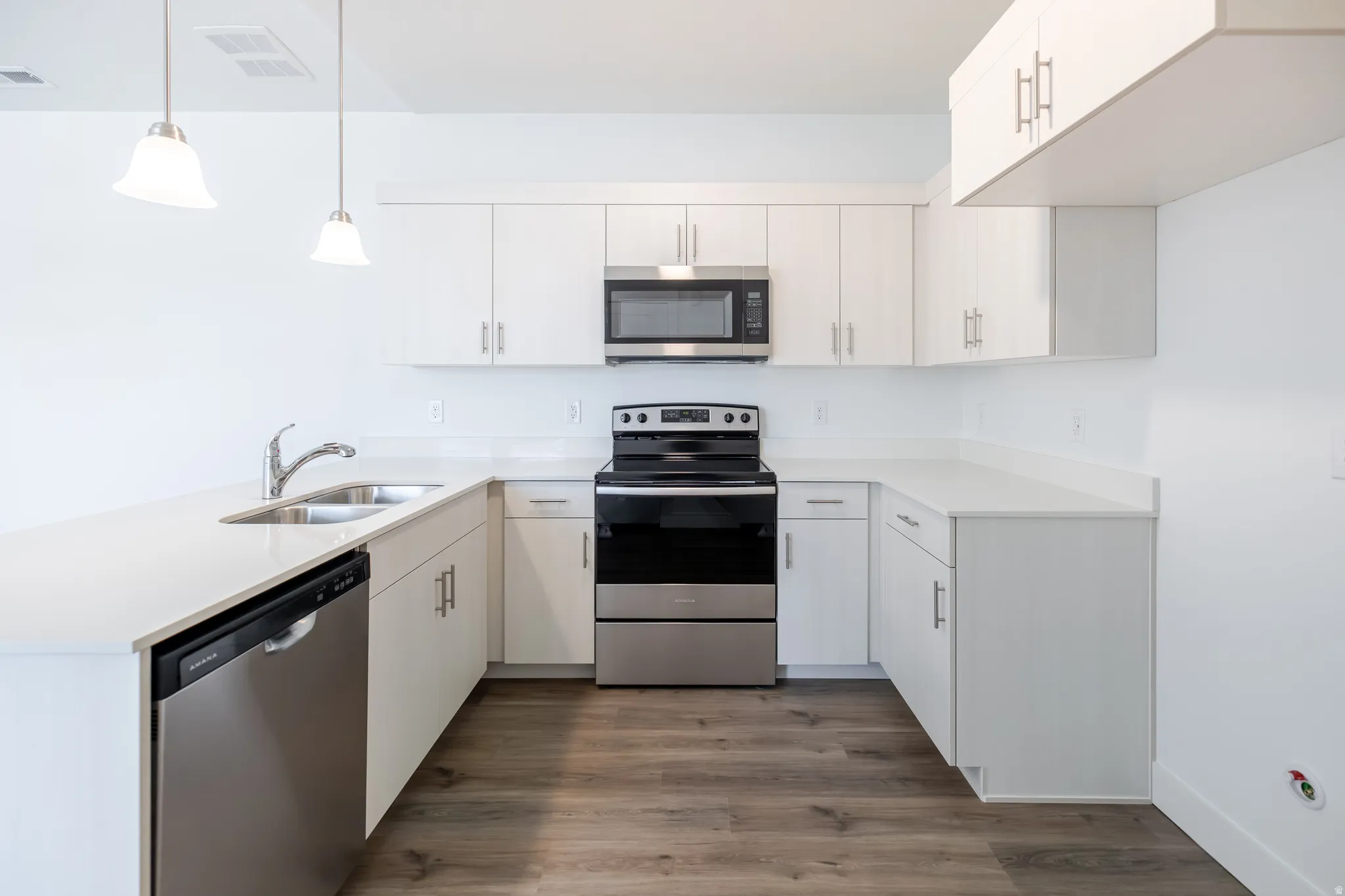 U-shaped kitchen featuring white cabinetry, stainless steel appliances, wood-finish flooring, and pendant lighting
