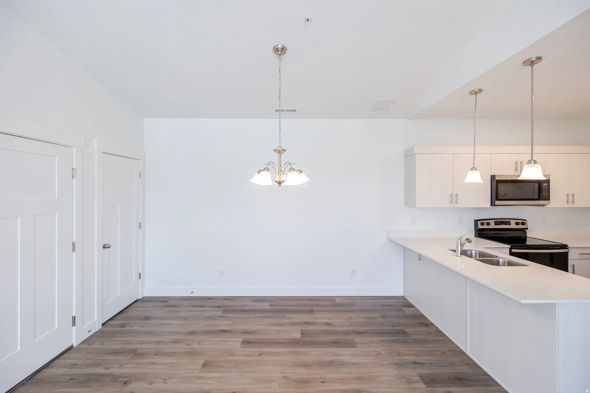 Kitchen featuring white cabinetry, stainless steel appliances, white countertops, and pendant lighting