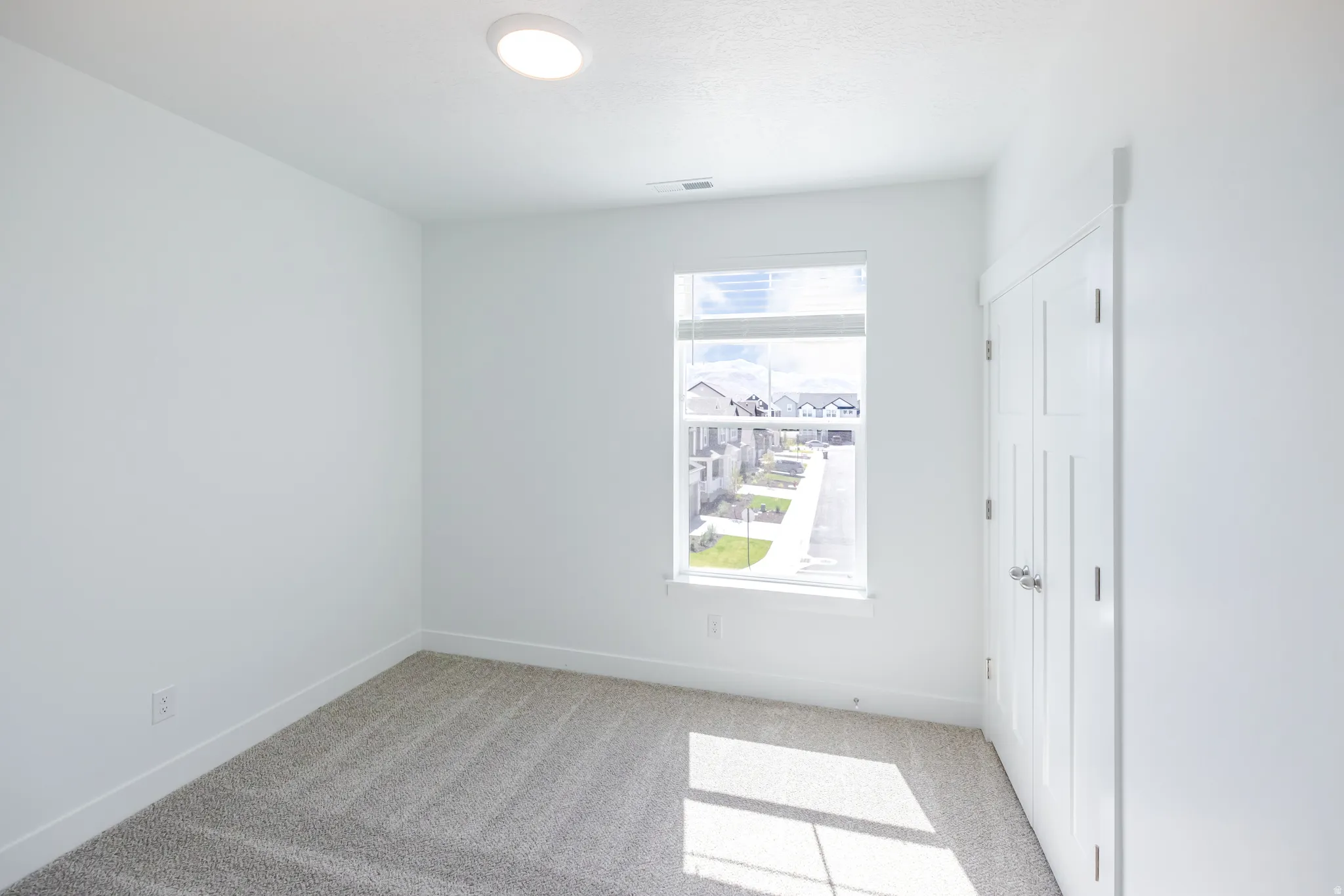 Neutral tone wall paint, flush mount ceiling lighting, carpet flooring, a window with horizontal blinds, and a built-in closet with double doors