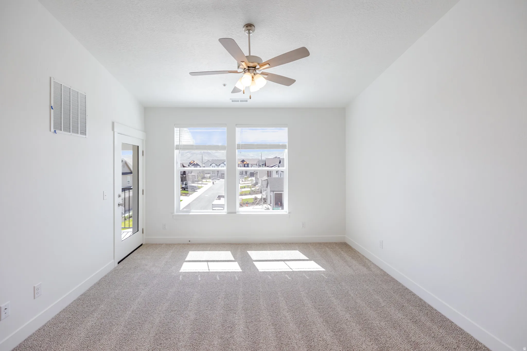 Neutral-toned carpeting with white walls, a ceiling fan with integrated lighting, and multiple windows