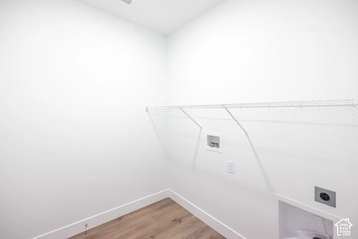 Dedicated laundry area featuring a wire shelf, wall connections, and wood-finish flooring