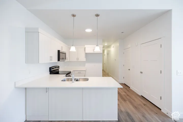 Contemporary kitchen featuring white cabinetry, integrated stainless steel sink, sleek countertops, and pendant lighting