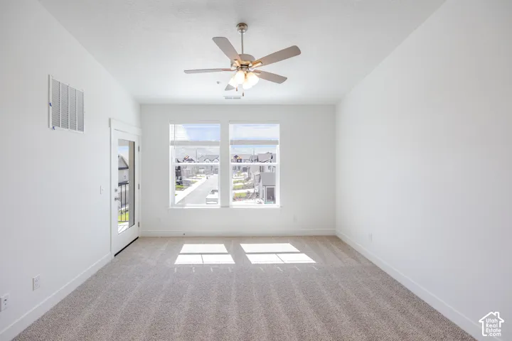 Neutral-toned carpeting with white walls, a ceiling fan with integrated lighting, and multiple windows