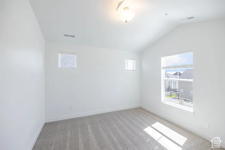 Vaulted ceiling room with neutral carpet, multiple windows, and a semi-flush mount light fixture