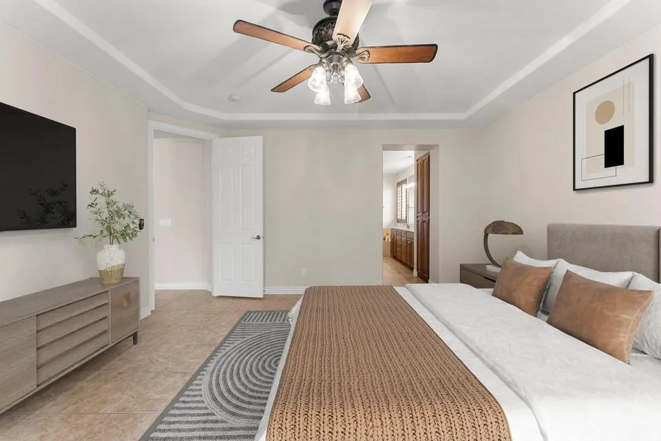 Bedroom featuring ensuite bathroom, a raised ceiling, light tile patterned flooring, and ceiling fan