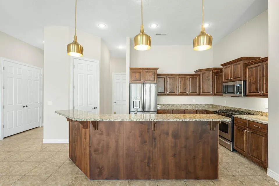Kitchen featuring light stone countertops, stainless steel appliances, light tile patterned floors, a kitchen island, and pendant lighting