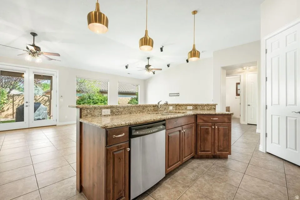 Kitchen featuring dishwasher, ceiling fan, light tile patterned floors, a center island with sink, and vaulted ceiling