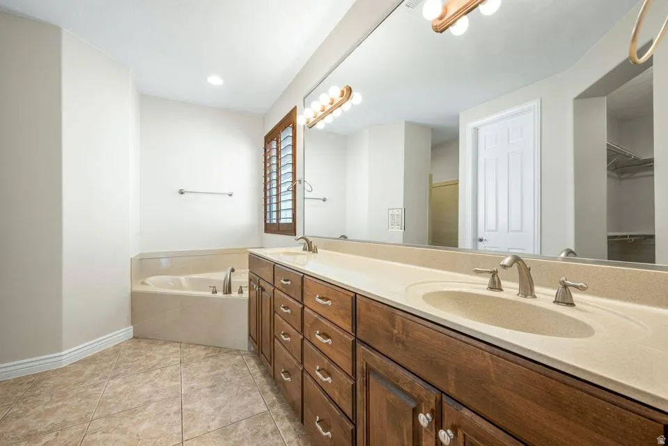 Full bathroom featuring a garden tub, double vanity, light tile patterned flooring, and a walk in closet