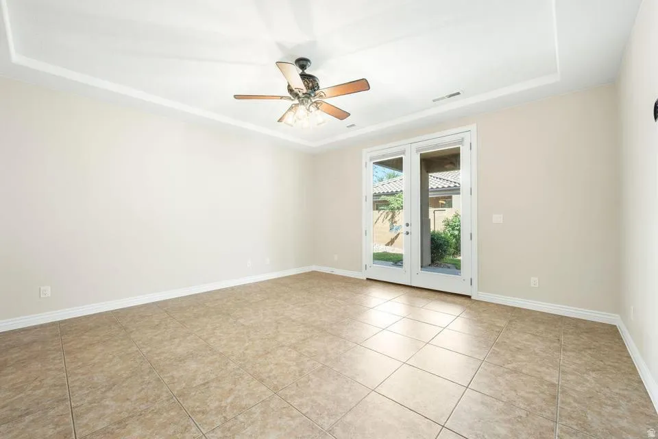 Empty room with a tray ceiling, a ceiling fan, and light tile patterned floors