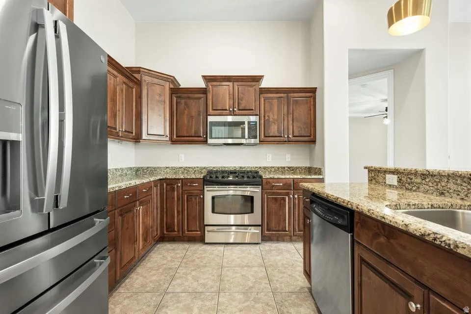 Kitchen featuring stainless steel appliances, light stone counters, light tile patterned flooring, ceiling fan, and dark wood finish cabinets