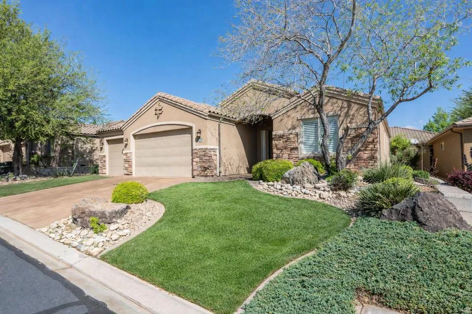 View of front of home featuring an attached garage, stone siding, concrete driveway, and a front lawn