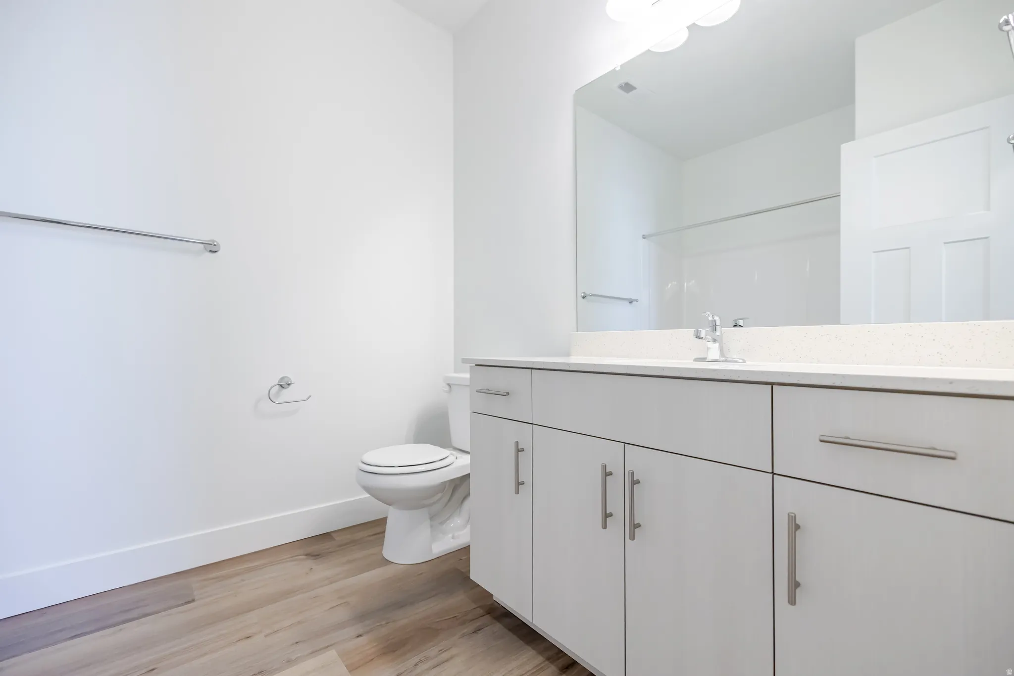 Wood-finish flooring, white vanity with ample storage, integrated sink, and broad wall mirror