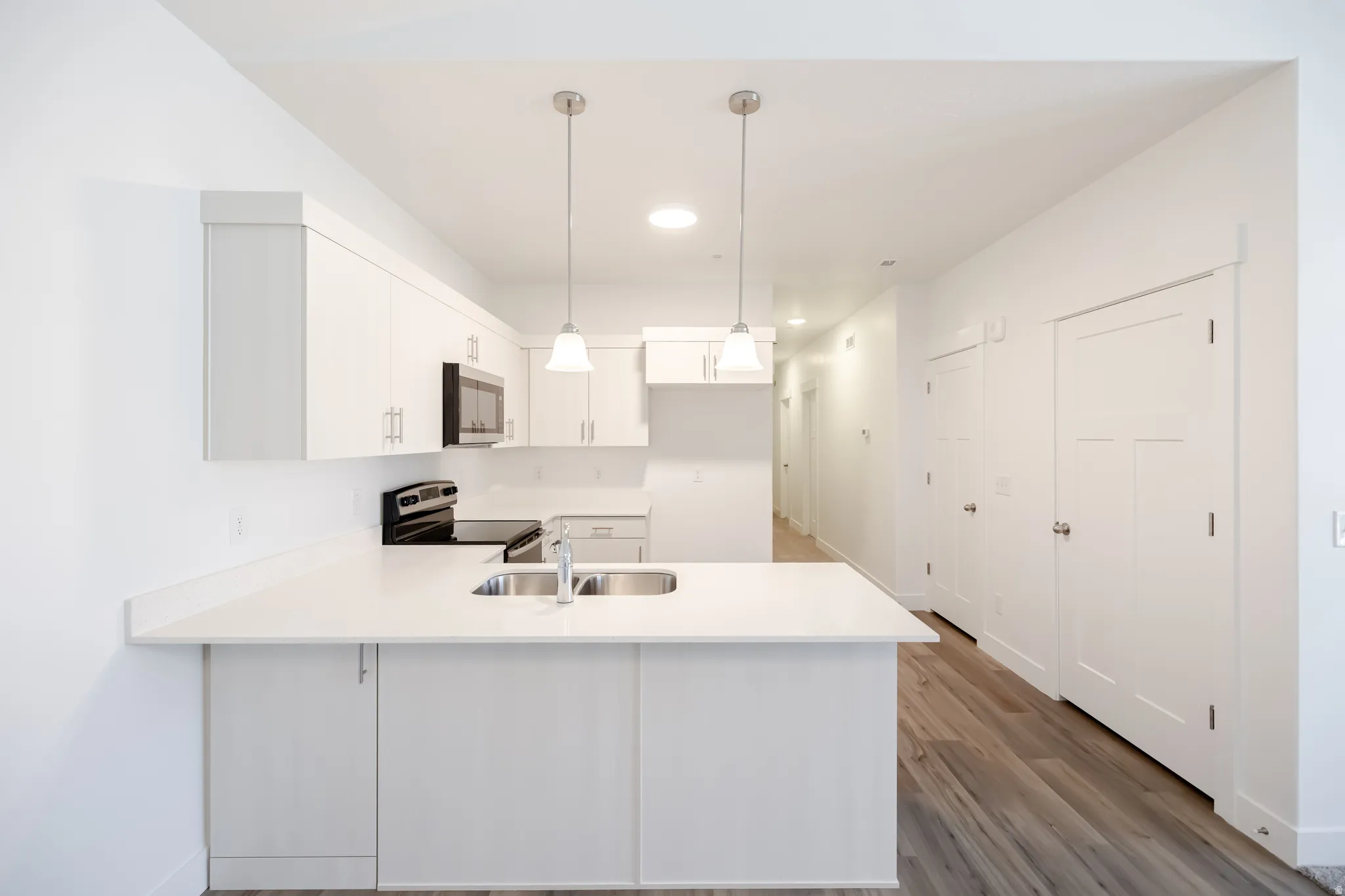 Kitchen featuring white cabinetry, stainless steel sink, built-in microwave, and pendant lighting