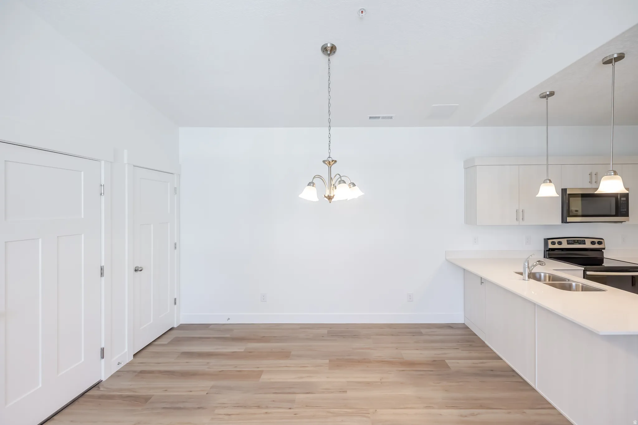 Open-concept dining area with wood-finish flooring, a multi-light chandelier, and white paneled doors