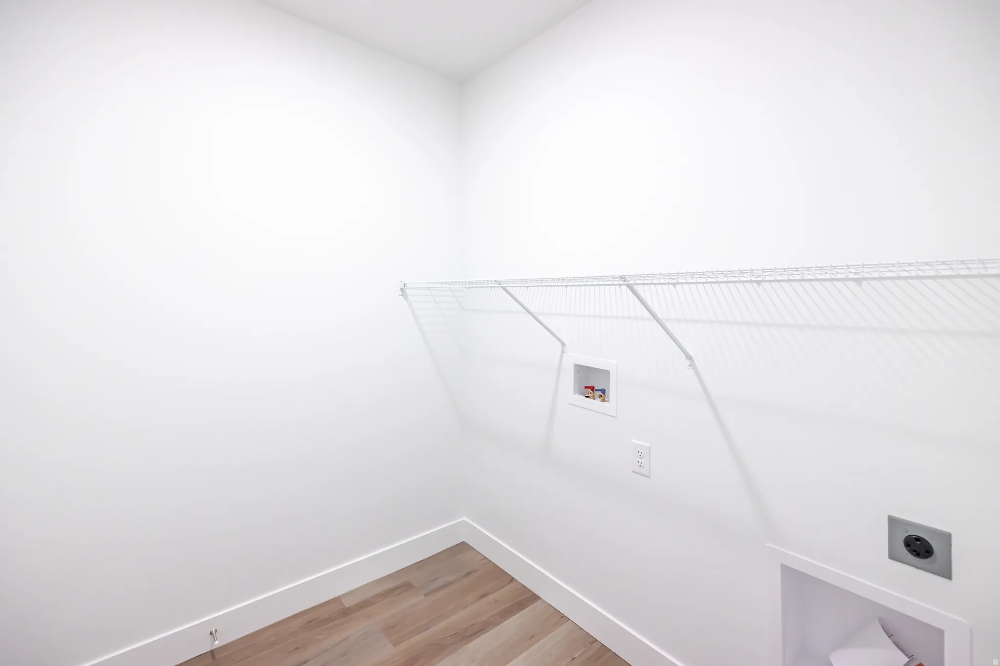 White walls with wood-finish flooring, featuring a built-in wire shelf, washing machine hookups, and dryer vent