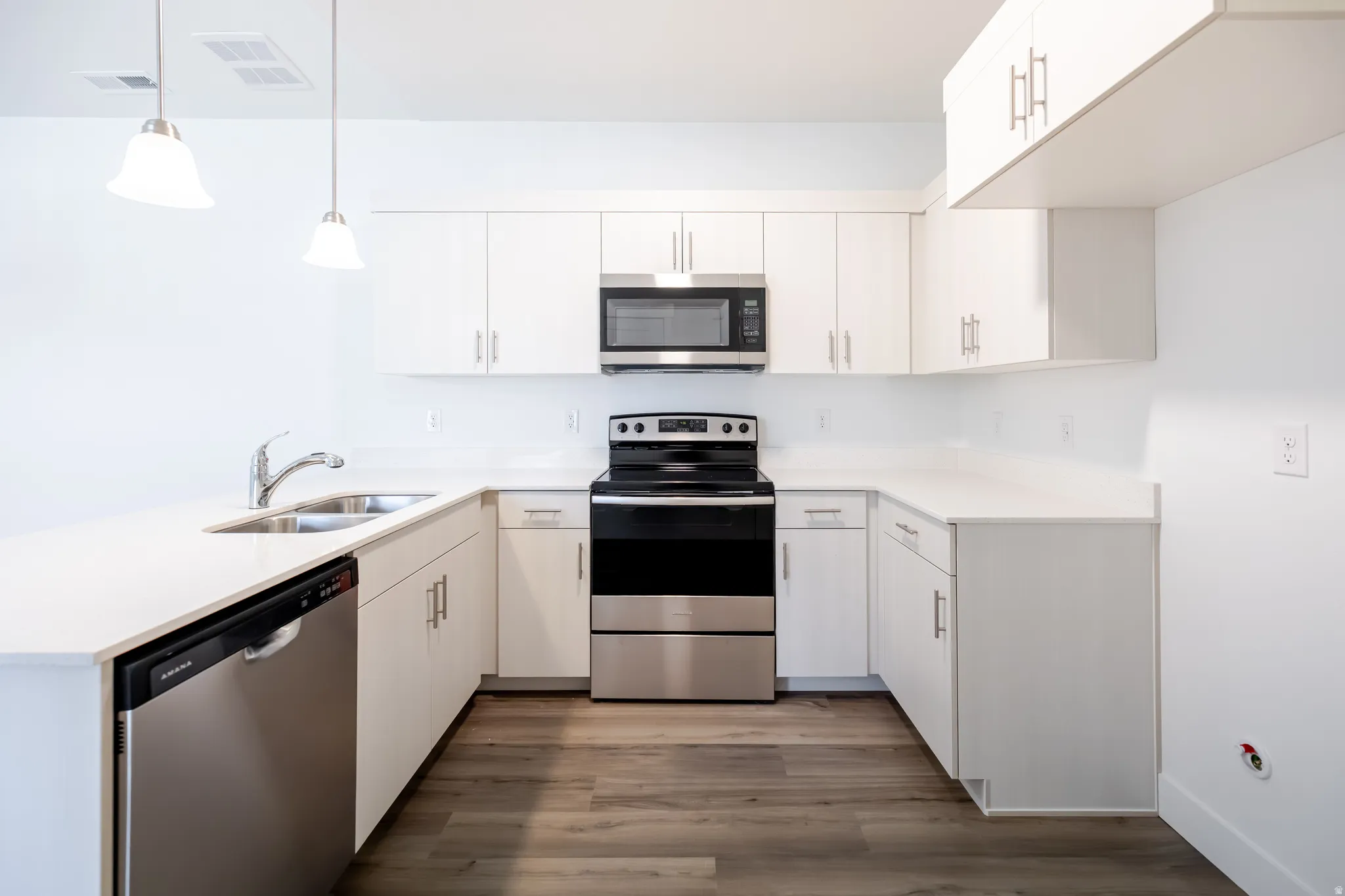 U-shaped kitchen featuring white cabinetry, stainless steel appliances, white countertops, a stainless steel sink, and wood-finish flooring