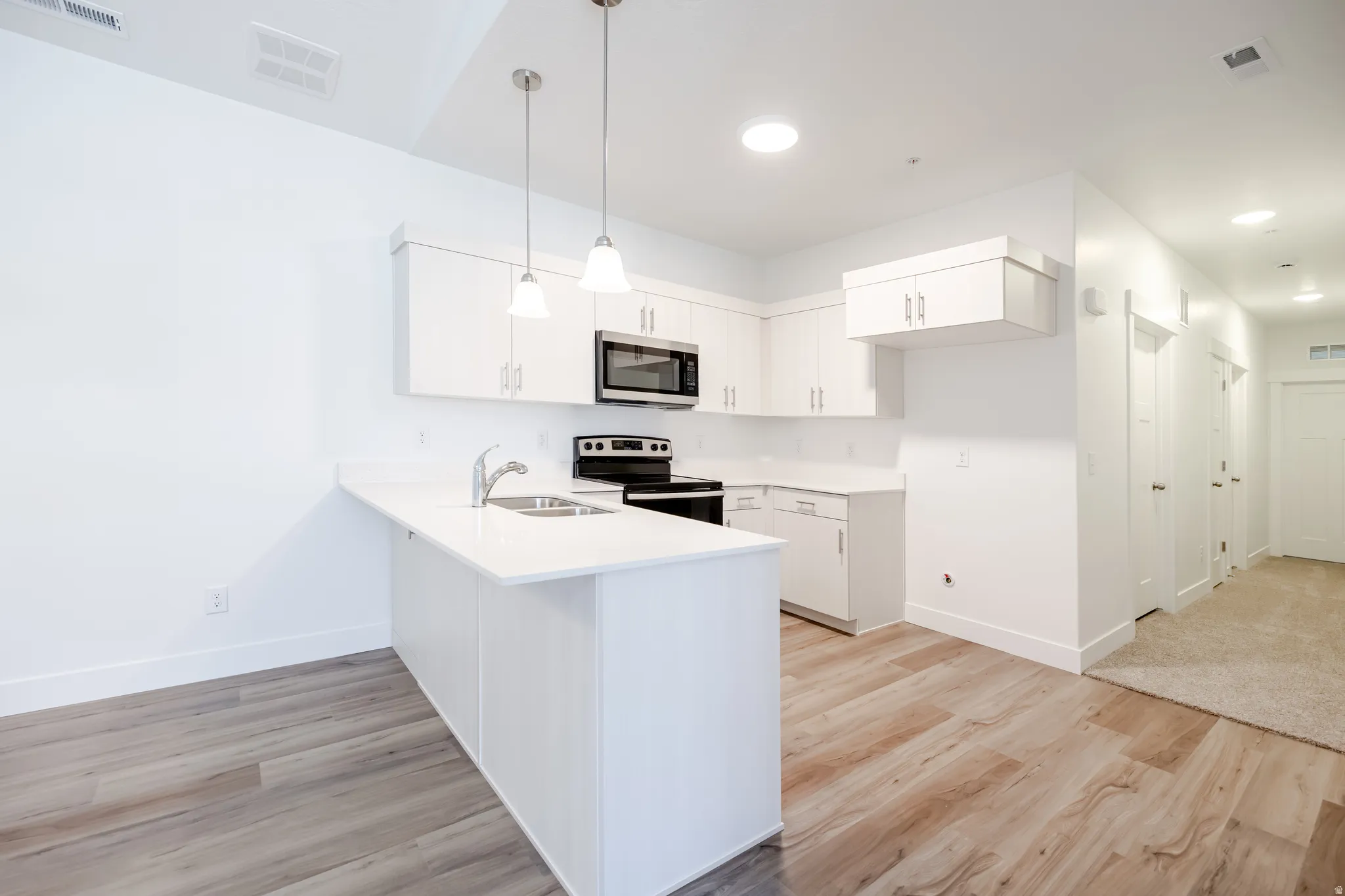 Kitchen featuring white cabinetry, light countertops, wood-finish flooring, stainless steel appliances, and pendant lighting over a breakfast bar