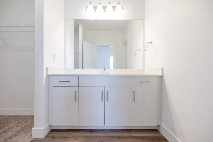 Vanity with integrated sink, white cabinetry, and a large wall-mounted mirror