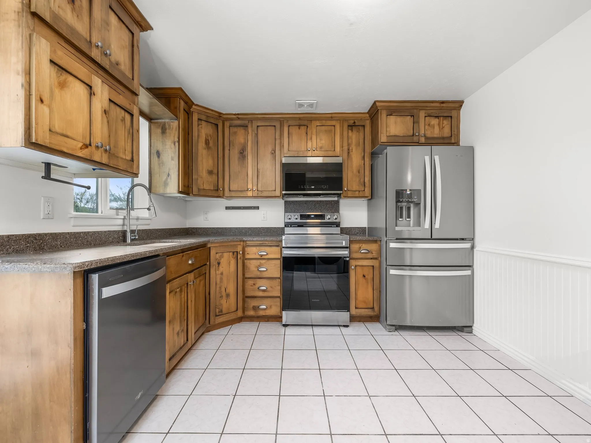 Kitchen featuring stainless steel appliances, wainscoting, wood finish cabinets, and light tile patterned flooring
