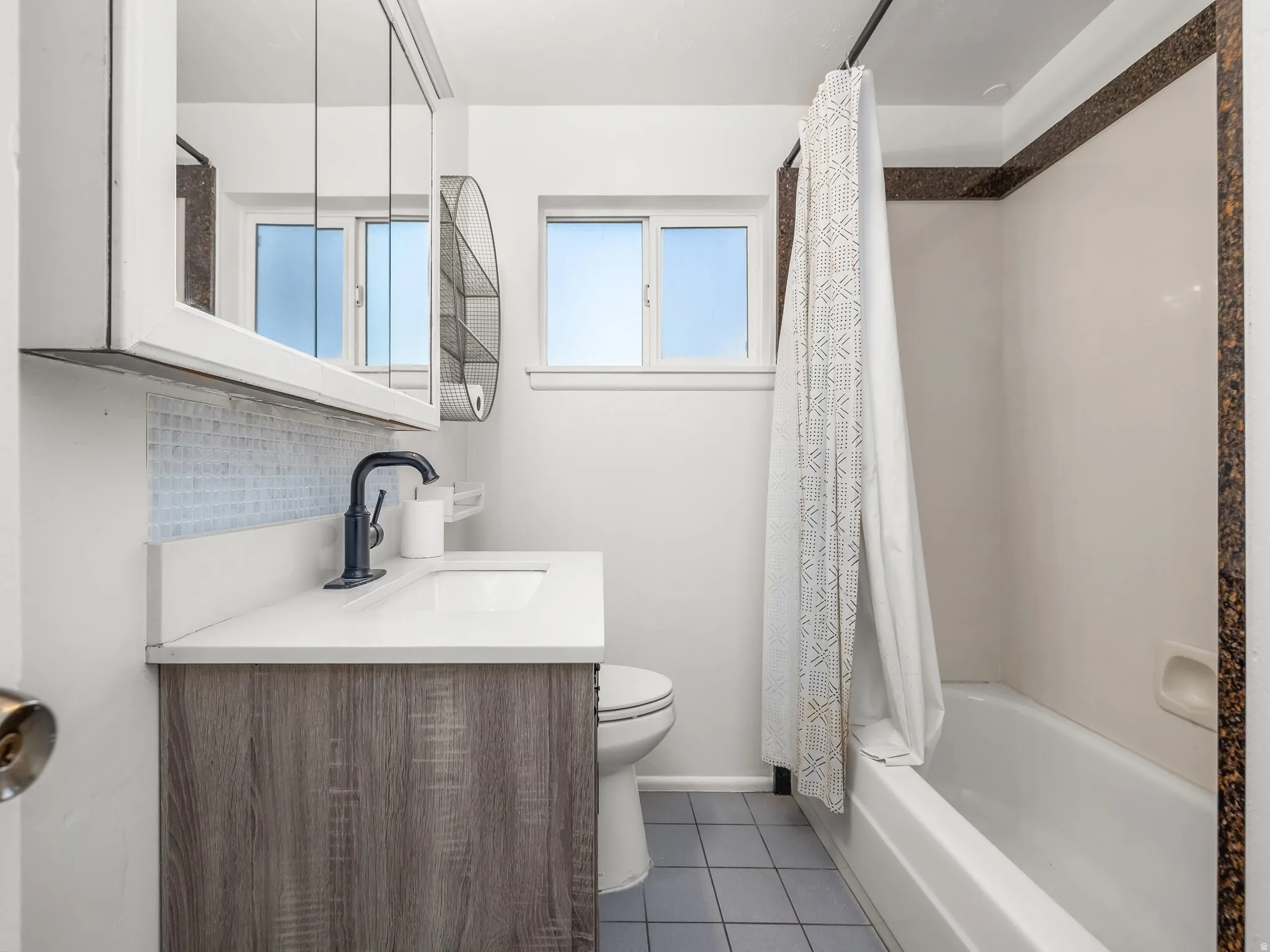 Full bathroom featuring backsplash, shower / bath combo with shower curtain, vanity, and dark tile patterned flooring