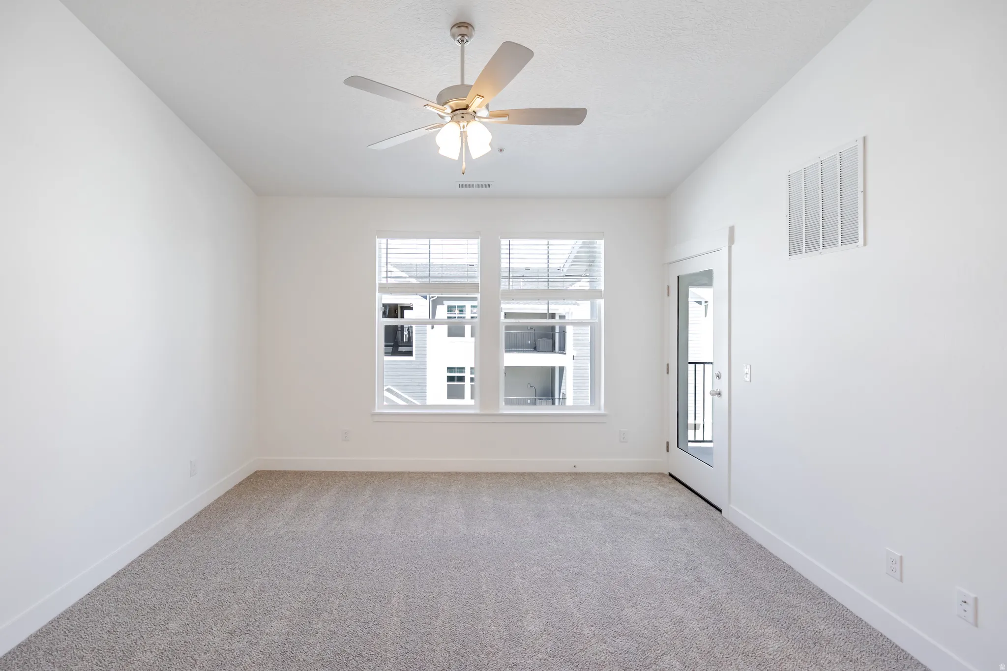 Recessed ceiling fan with integrated lighting, two large windows with blinds, a glass-paneled exterior door, and light gray carpeting