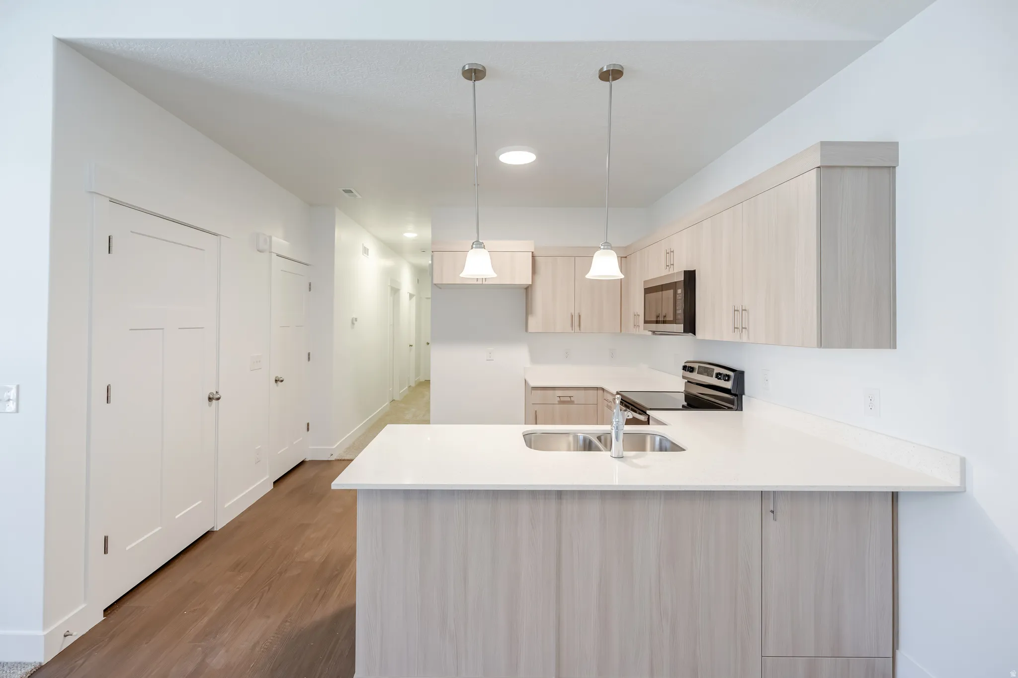 Kitchen featuring light wood-finish cabinetry, white countertops, stainless steel sink with chrome faucet, and recessed lighting