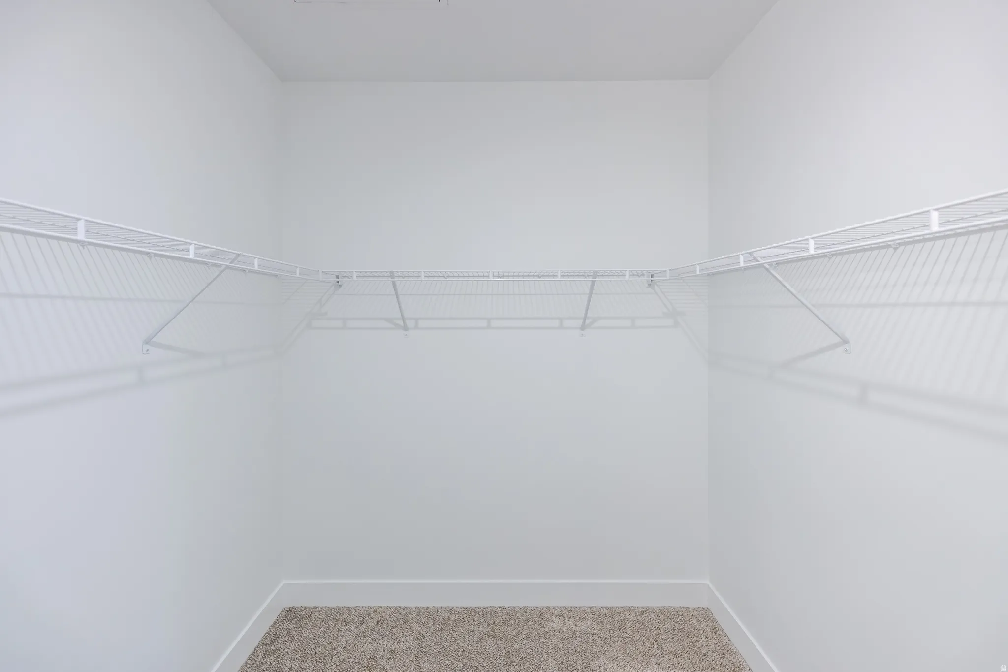 Built-in wire shelving with corner wrap-around configuration, neutral carpet flooring, and white wall finishes