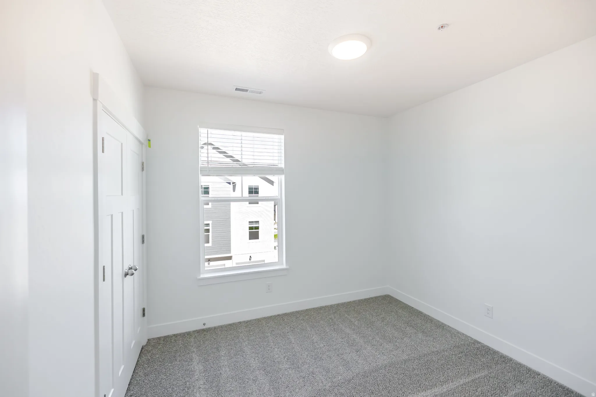 Plush carpet flooring, white interior walls, a window with blinds, and a flush-mount ceiling light fixture