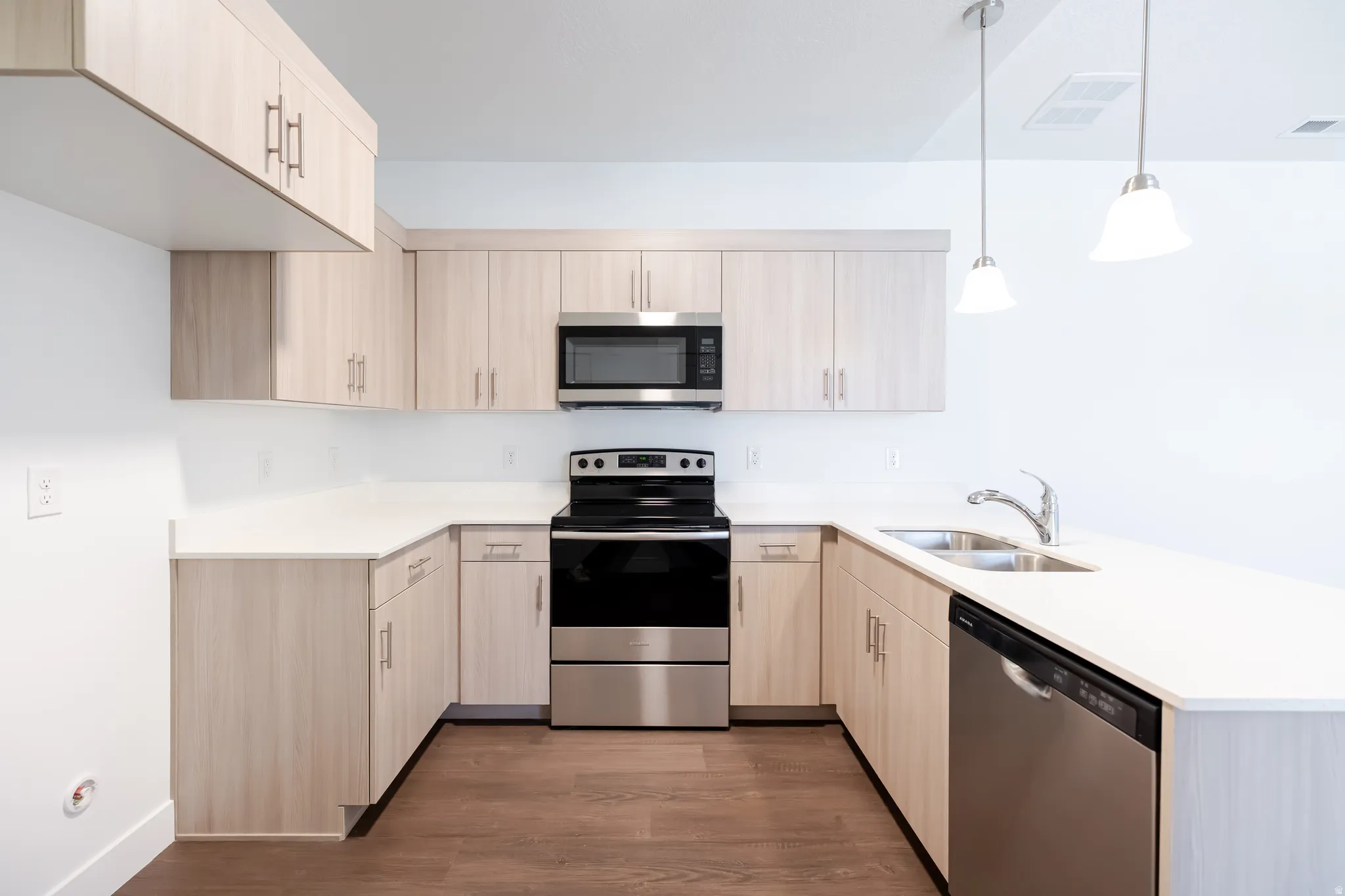 U-shaped kitchen with light wood-finish cabinetry, stainless steel appliances, white countertops, and wood-finish flooring