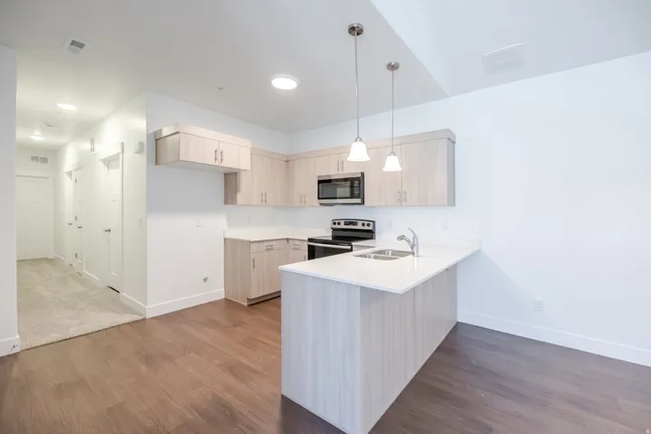 Kitchen with light wood-finish cabinetry, white countertops, built-in microwave, and stainless steel sink