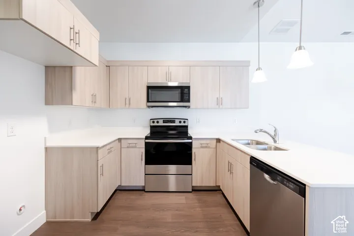 U-shaped kitchen with light wood-finish cabinetry, stainless steel appliances, white countertops, and wood-finish flooring