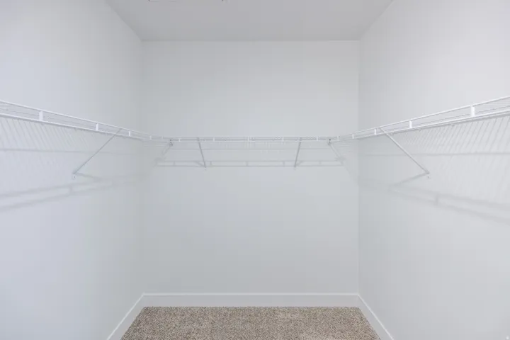 Built-in wire shelving with corner wrap-around configuration, neutral carpet flooring, and white wall finishes