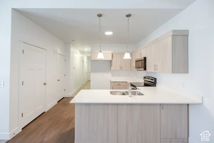 Kitchen featuring light wood-finish cabinetry, white countertops, stainless steel sink with chrome faucet, and recessed lighting