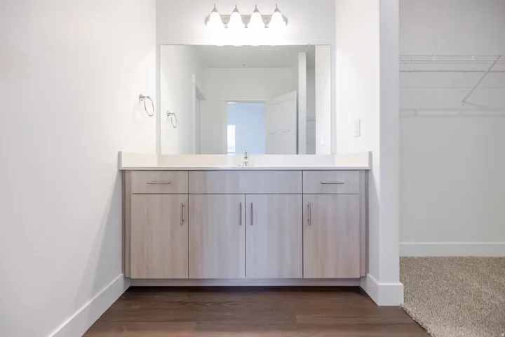 Light wood-finish vanity with a light-toned countertop, undermount sink, and a framed mirror