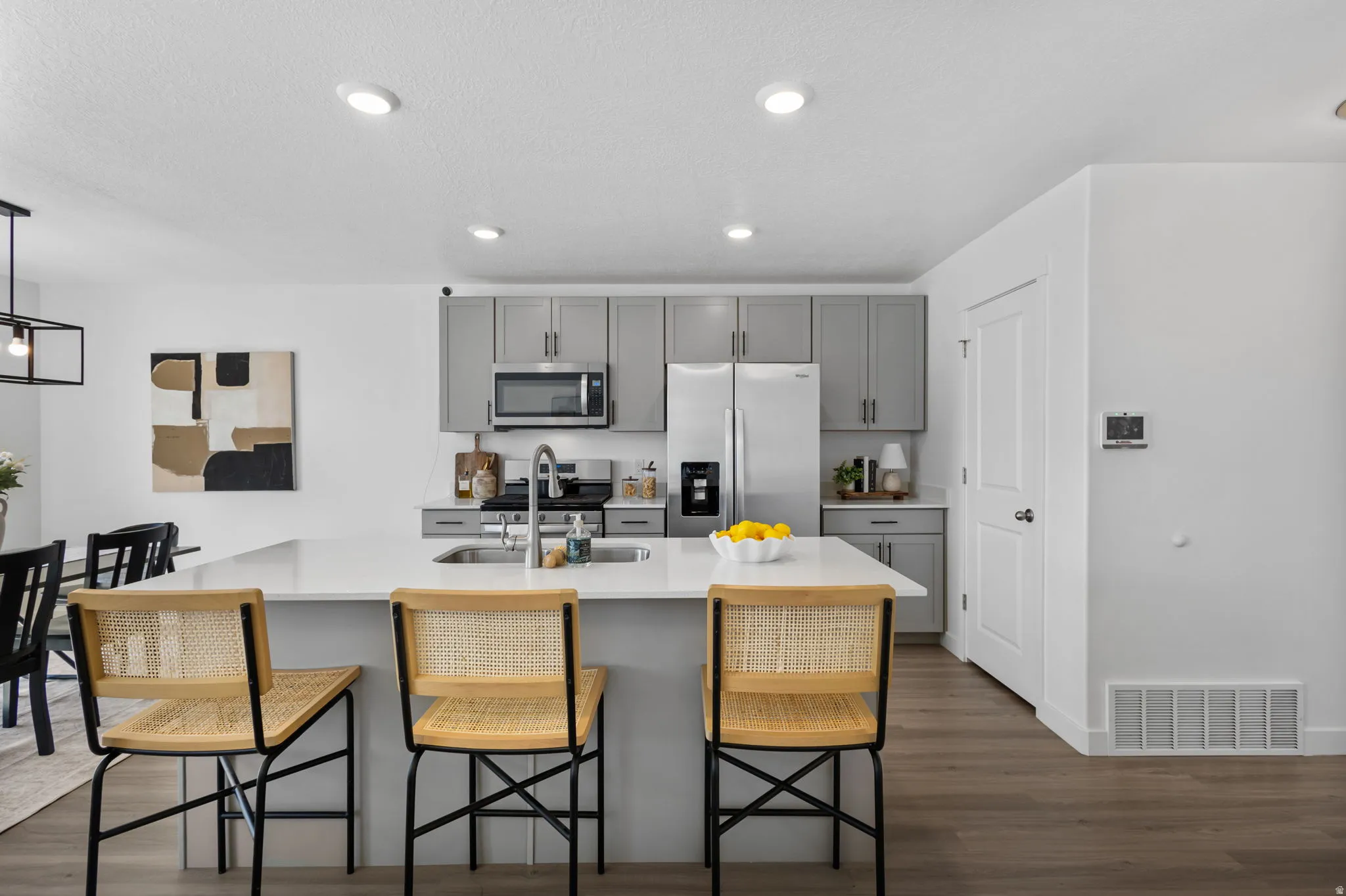 Kitchen with stainless steel appliances, gray cabinetry, dark wood-style floors, a kitchen breakfast bar, and an island with sink
