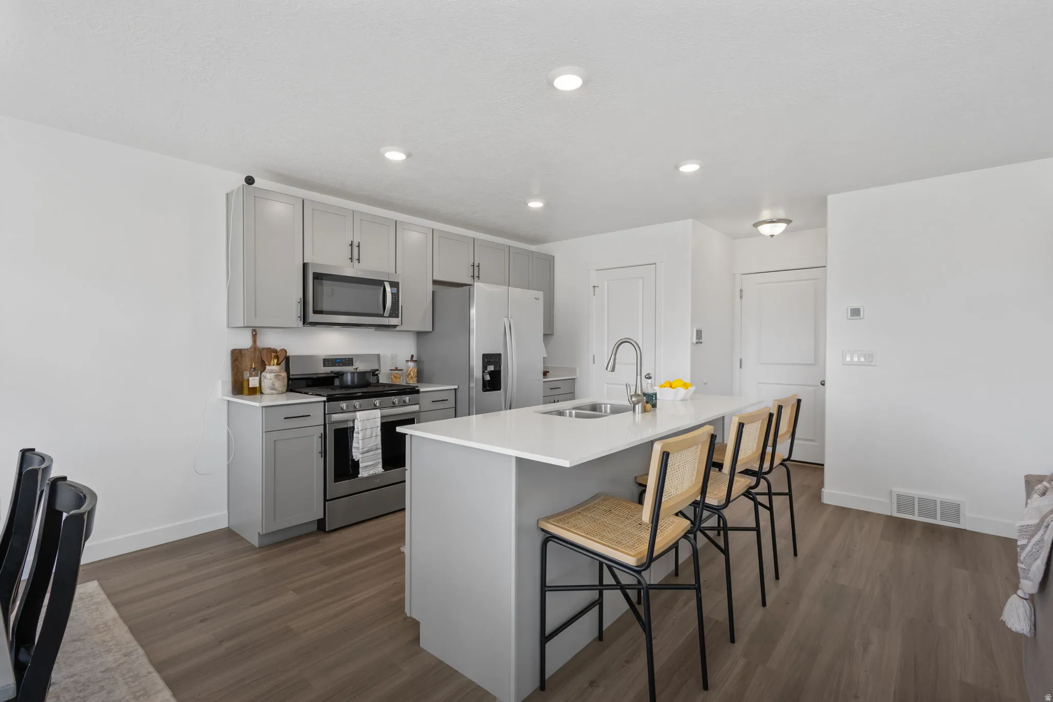 Kitchen with gray cabinetry, stainless steel appliances, a kitchen bar, dark wood finished floors, and a center island with sink