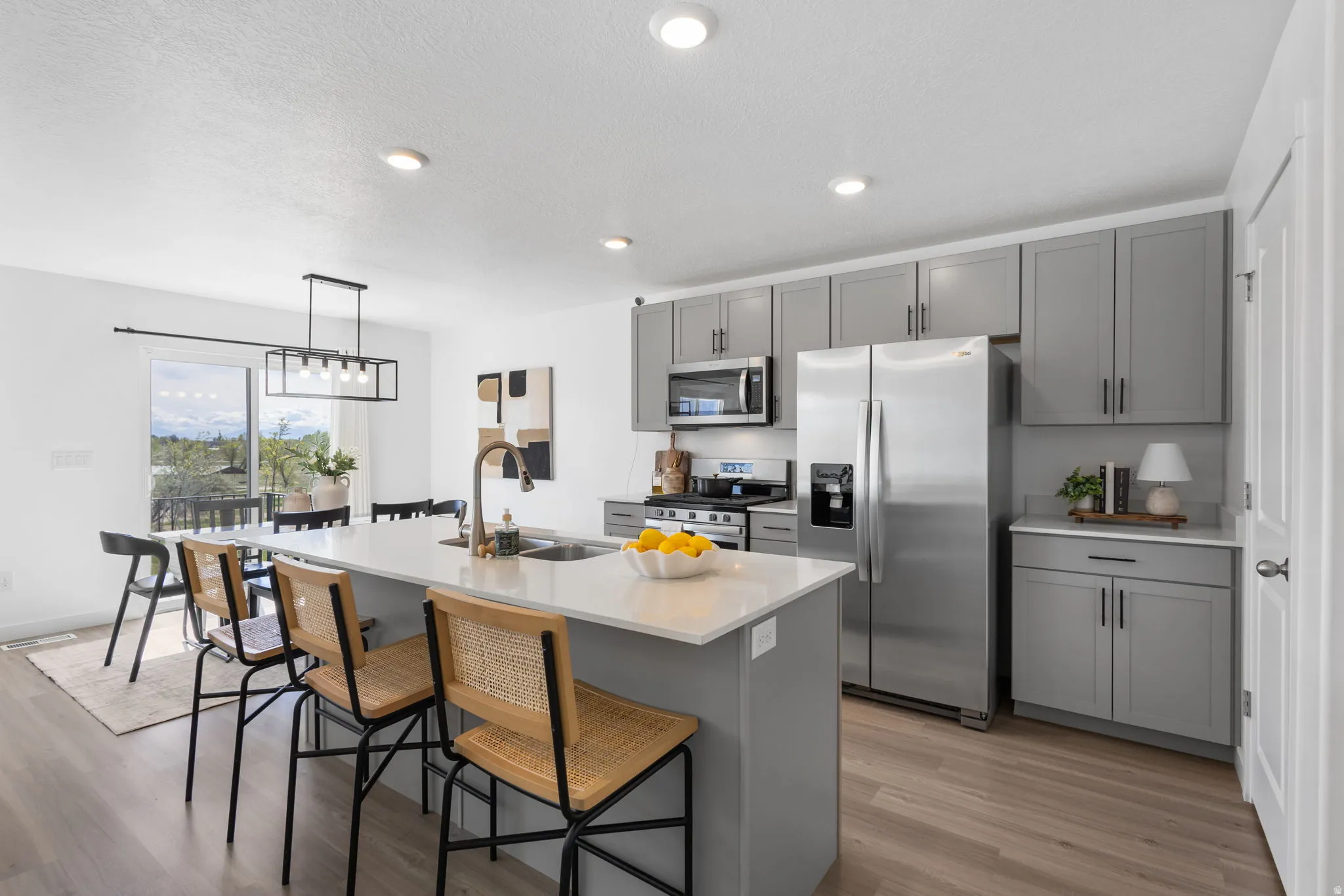 Kitchen featuring gray cabinets, stainless steel appliances, a kitchen breakfast bar, light wood-type flooring, and an island with sink