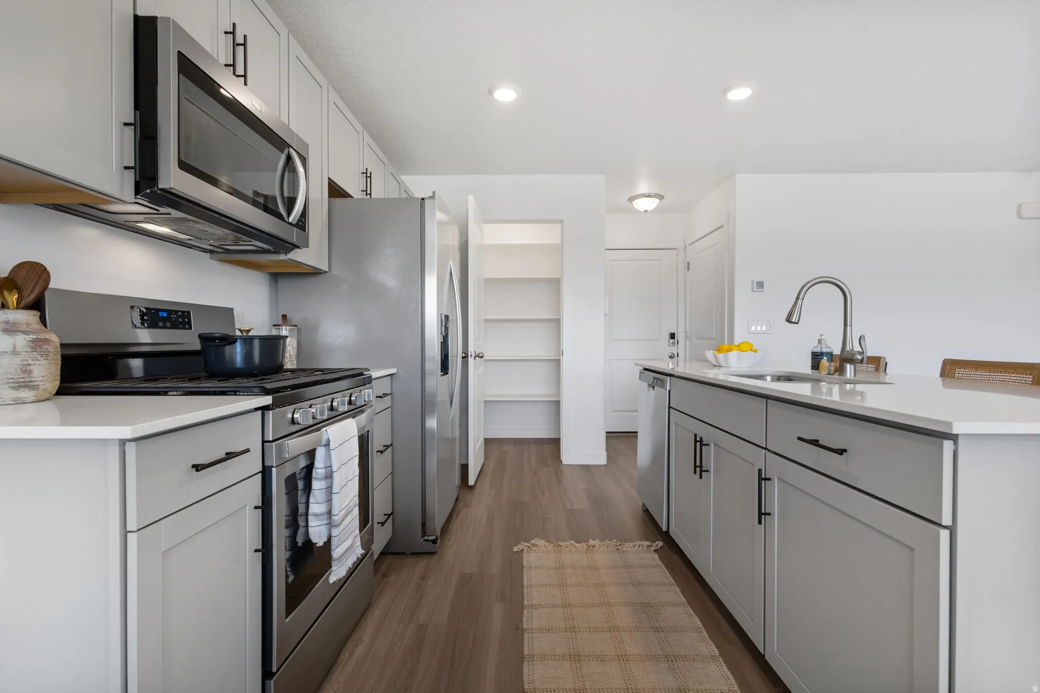 Kitchen featuring stainless steel appliances, dark wood-type flooring, an island with sink, light stone counters, and gray cabinets