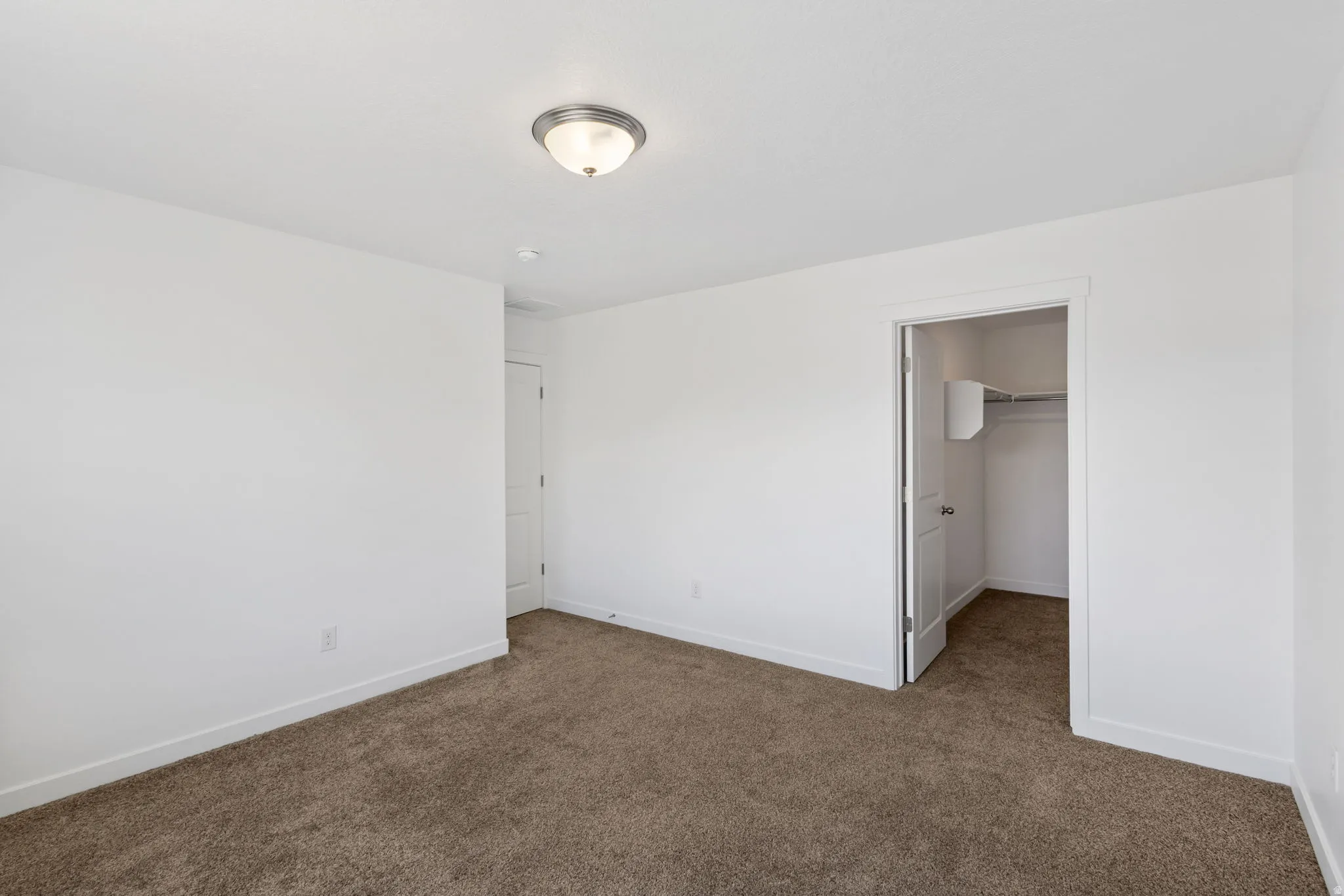 Unfurnished bedroom with a walk in closet and dark colored carpet