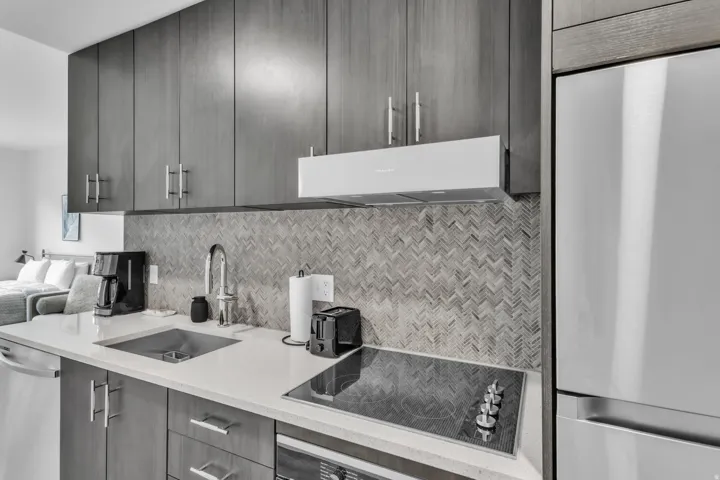 Kitchen with stainless steel appliances, light stone countertops, decorative backsplash, modern cabinets, and extractor fan
