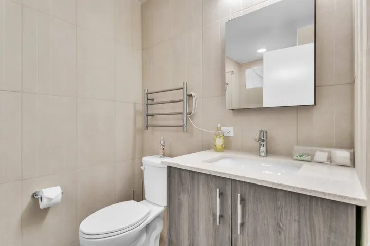 Bathroom featuring tile walls, vanity, radiator heating unit, and recessed lighting