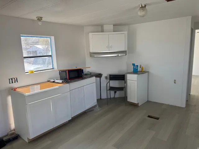 Kitchen with white cabinetry, light wood-style flooring, and black microwave