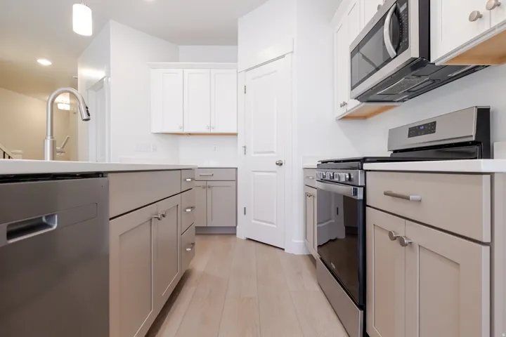 Kitchen featuring light wood-finish flooring, two-tone cabinetry, stainless steel appliances, and a kitchen island with a single basin sink