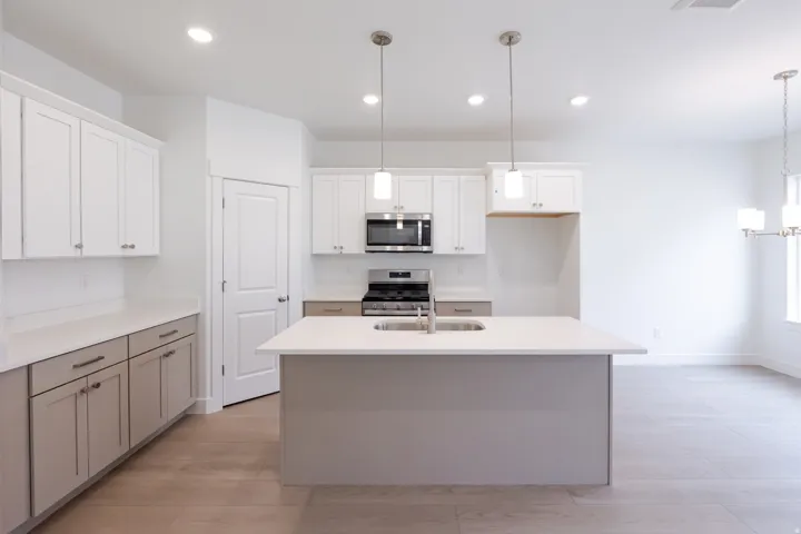 Kitchen featuring white shaker cabinetry, stainless steel appliances, a center island with sink, quartz countertops, and wood-finish flooring