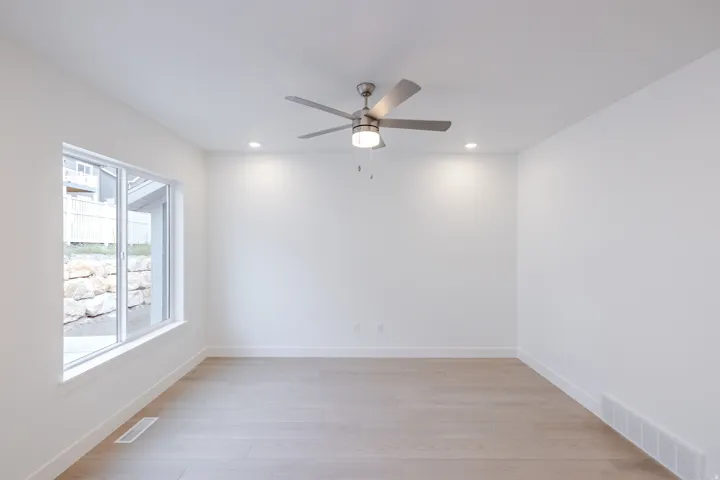 Recessed lighting, ceiling fan with brushed nickel finish, large window, light wood-finish flooring, and crisp white walls