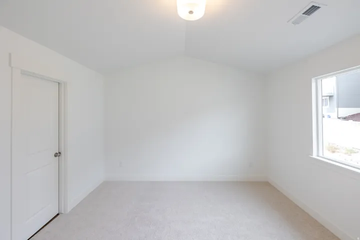 Vaulted ceiling with flush-mount lighting, light-toned carpeting, and a white framed window