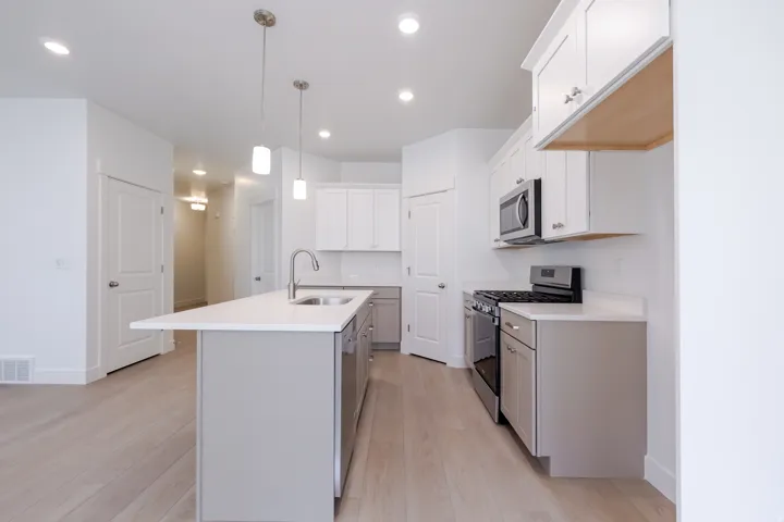 Kitchen featuring an island with a stainless steel sink, pendant lighting, built-in microwave, white upper cabinetry, and light wood-finish flooring