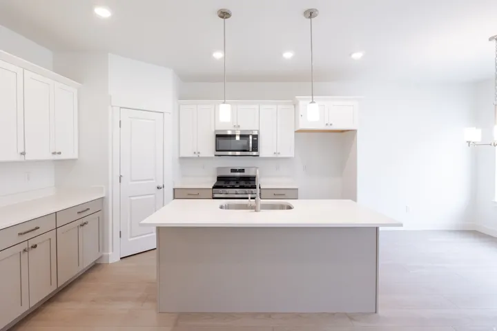 Kitchen featuring a central island with an undermount sink, pendant lighting, stainless steel appliances, white cabinetry, and wood-finish flooring